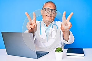 Senior handsome man with gray hair wearing doctor uniform working using computer laptop smiling looking to the camera showing