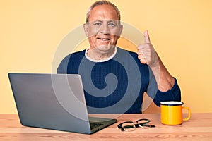 Senior handsome man with gray hair working at the office with laptop smiling happy and positive, thumb up doing excellent and