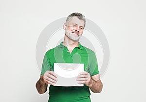 Senior handsome man with mustache and beard wearing green shirt holds the white sign in a studio