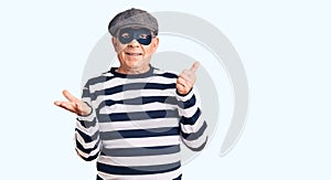 Senior handsome man wearing burglar mask and t-shirt showing palm hand and doing ok gesture with thumbs up, smiling happy and