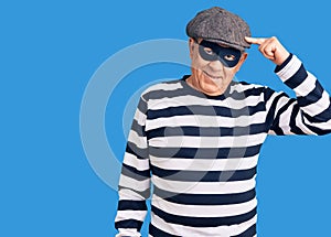 Senior handsome man wearing burglar mask and t-shirt smiling pointing to head with one finger, great idea or thought, good memory