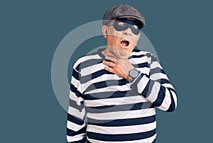 Senior handsome man wearing burglar mask and t-shirt touching painful neck, sore throat for flu, clod and infection