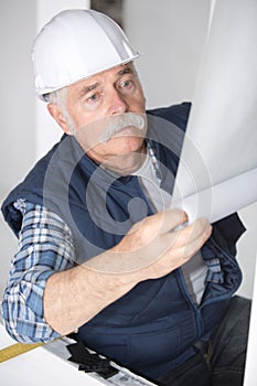 Senior handyman putting up wallpaper on white walls