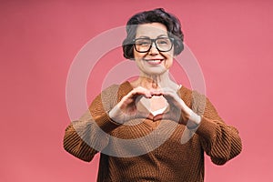 Senior happy aged business woman wearing glasses. Beautiful old woman, grandmother looking at camera and smiling. Isolated on pink