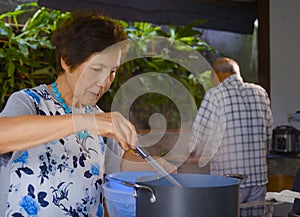 senior happy and beautiful retired Asian Japanese couple cooking together at home kitchen enjoying preparing meal relaxed