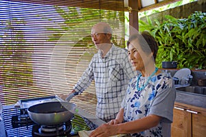 Senior happy and beautiful retired Asian Japanese couple cooking together at home kitchen enjoying preparing meal relaxed in aged