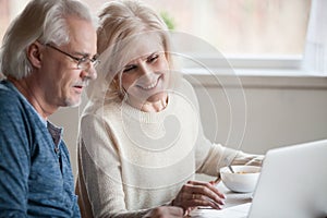 Senior happy couple enjoying using laptop eating breakfast toget