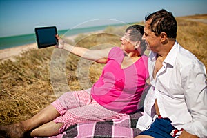 Senior happy couple having fun using digital tablet pc at beach during moment of relax