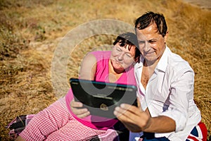 Senior happy couple having fun using digital tablet pc at beach during moment of relax