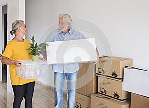 Senior happy couple holding moving boxes entering in the new empty apartment - concept of active elderly people and new beginning