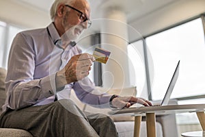 Senior happy smiling handsome man sitting at his home or office using laptop computer and credit card for online shopping web