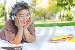 Senior happy woman listening music at park by wear headphone and using digital tablet Elderly woman get relax and happy when old