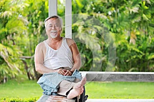 Senior Asian man wearing only sando while sitting at the balcony surrounded by garden plant in his home photo