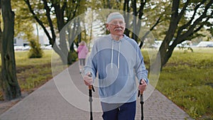 Senior healthy retired man grandfather training Nordic walking use ski trekking poles in summer park