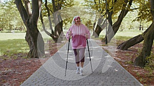 Senior healthy retired woman grandmother training Nordic walking in summer park, ski trekking poles