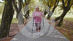 Senior healthy retired woman grandmother training Nordic walking in summer park, ski trekking poles