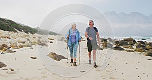 Senior hiker couple with backpack and hiking poles talking to each other and walking while hiking