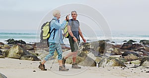 Senior hiker couple with backpack and hiking poles talking to each other and walking while hiking