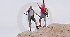 Senior hiker couple with backpack and trekking poles standing with their arms wide open on the rocks