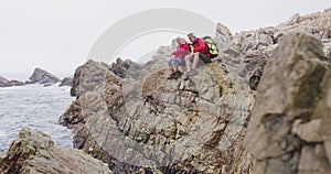 Senior hiker couple with backpacks sitting and talking on the rocks while hiking near sea shore.