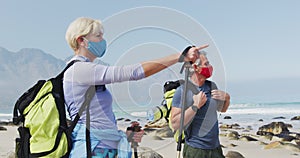 Senior hiker couple wearing face masks with backpacks and hiking poles pointing towards a direction