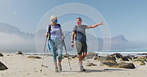 Senior hiker couple wearing face masks with backpacks and hiking poles pointing towards a direction
