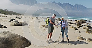 Senior hiker couple wearing face masks with backpacks and hiking poles reading map while hiking