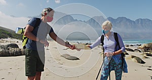 Senior hiker couple wearing face masks with backpacks and hiking poles reading maps while hiking