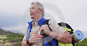 Senior hiker man with backpack standing and looking around while trekking in the mountains.