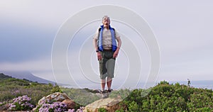 Senior hiker man standing with his arms wide open standing on a rock while trekking in the mountains