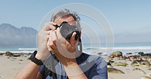 Senior hiker man taking pictures using digital camera on the beach.