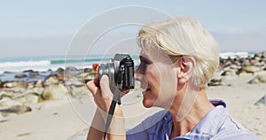 Senior hiker woman taking pictures using digital camera on the beach.