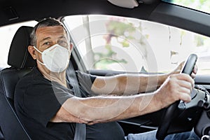 Senior in his 70s driving car wearing a face mask