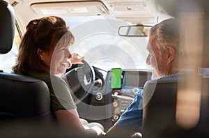 Senior Hispanic Couple On Drive Through Countryside Using Sat Nav On Mobile Phone