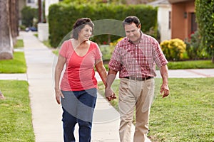 Senior Hispanic Couple Walking Along Sidewalk Together