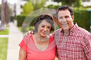 Senior Hispanic Couple Walking Along Sidewalk Together