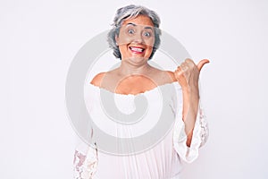 Senior hispanic grey- haired woman wearing casual clothes smiling with happy face looking and pointing to the side with thumb up