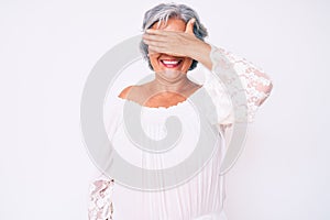 Senior hispanic grey- haired woman wearing casual clothes smiling and laughing with hand on face covering eyes for surprise