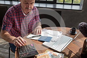 Senior hispanic man busy doing calculation, counting money and bills at home.