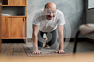 Senior hispanic man practices yoga asana marjariasana or cat-cow pose at home.