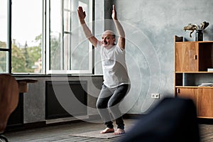 Man practicing yoga indoors at living room doing Chair pose or Utkatasana