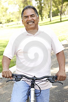 Senior Hispanic Man Riding Bike In Park