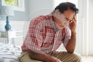 Senior Hispanic Man Sitting On Bed Suffering With Depression