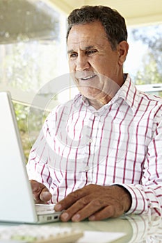 Senior Hispanic Man Using Laptop In Home Office