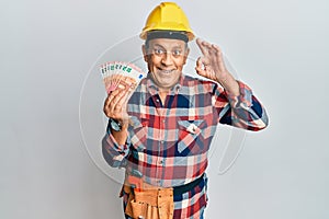 Senior hispanic man wearing handyman uniform and hardhat doing ok sign with fingers, smiling friendly gesturing excellent symbol