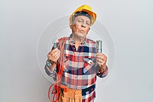 Senior hispanic man wearing handyman uniform holding led lightbulb and incandescent bulb looking at the camera blowing a kiss