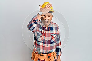 Senior hispanic man wearing handyman uniform surprised with hand on head for mistake, remember error