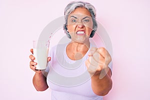 Senior hispanic woman holding glass of milk annoyed and frustrated shouting with anger, yelling crazy with anger and hand raised