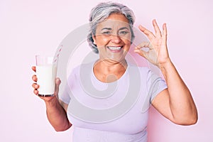 Senior hispanic woman holding glass of milk doing ok sign with fingers, smiling friendly gesturing excellent symbol