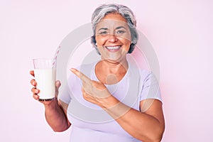 Senior hispanic woman holding glass of milk smiling happy pointing with hand and finger